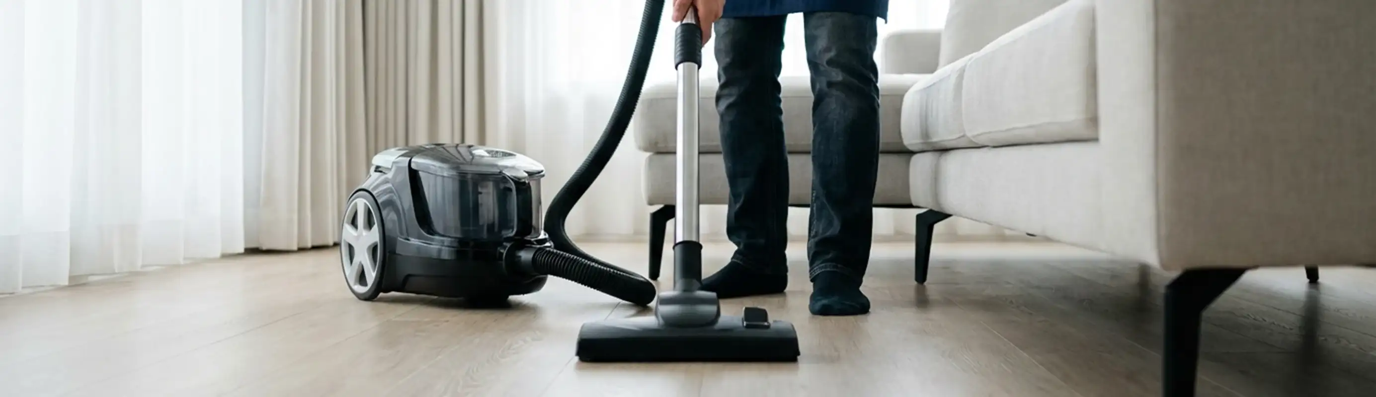 Professional house cleaner vacuuming a living room floor with a canister vacuum cleaner, Portland, OR.