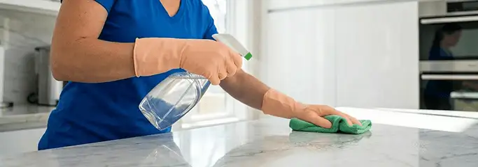 Maid service worker spraying and wiping a kitchen countertop with a microfiber cloth for sanitizing, Portland, OR.