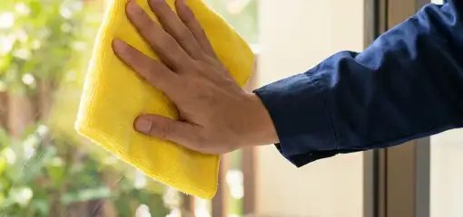 House cleaner wiping a glass window with a yellow microfiber cloth for streak-free cleaning, Portland, OR.